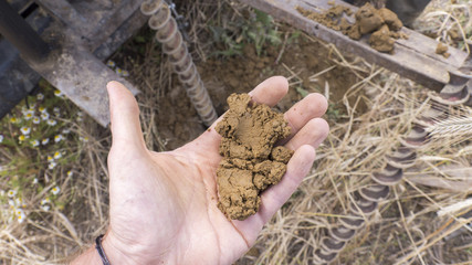 a sample of sandy loam on the hand - a drills and a hole in the background