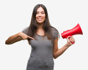 Young hispanic woman holding megaphone with surprise face pointing finger to himself