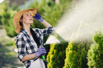 Beautiful young gardener woman watering garden in hot summer day