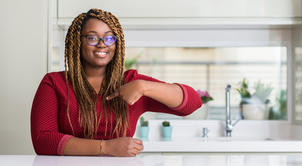 African american woman sitting at home with surprise face pointing finger to himself