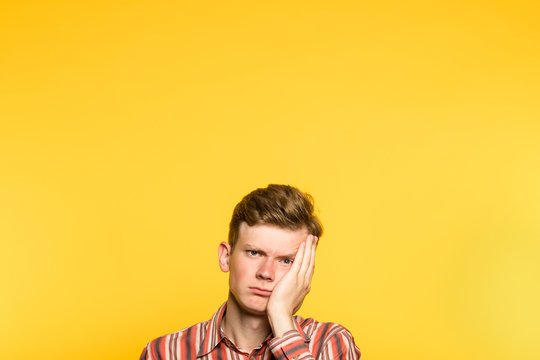 bored disinterested weariful indifferent unenthusiastic man. portrait of a young guy on yellow background popping up or peeking out from the bottom. copy space for advertisement.