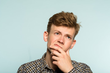 puzzled confused man scratching his chin thinking of smth looking up. portrait of a young guy on light background. emotion facial expression. feelings and people reaction concept.