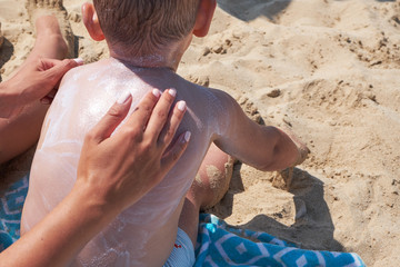 mother is putting on boy back a sunscreen on the beach.