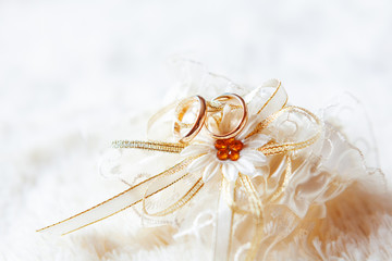 Golden wedding rings on bridal decorative garter with shiny rhinestones. Wedding details, symbol of love and marriage.