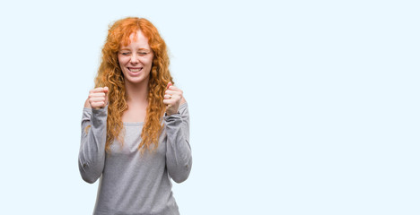 Young redhead woman excited for success with arms raised celebrating victory smiling. Winner concept.