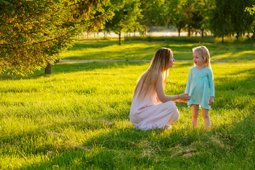 Game of tag .cute little blonde girl in a blue dress with beautiful long-haired mother having fun and playing catch-up hide and seek in summer day in field greens grass . happy children's Day