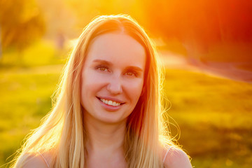 portrait of beautiful blonde long-haired woman having fun toothy smile in summer park against the background of sunset rays of the sun