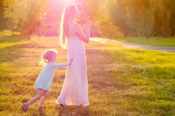 Fototapeta na wymiar Game of tag .cute little blonde girl daughter in a blue dress with beautiful long-haired mother having fun and playing catch-up in summer day in field greens and grass background. happy children's Day