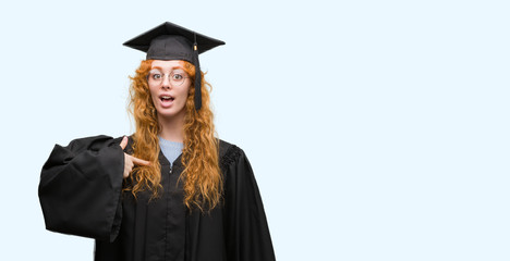 Young redhead student woman wearing graduated uniform with surprise face pointing finger to himself