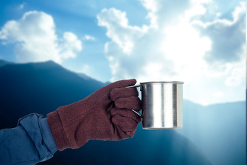 a mug of coffee in hand with a glove on the background of a beautiful mountain landscape