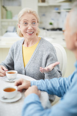 Happy mature blond woman explaining something to her husband by breakfast in the kitchen