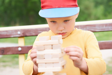 Caucasian kid is playing wood blocks tower game for practicing physical and mental skill. Emotional...