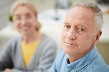 Senior man and his happy wife on background looking at camera while staying at home