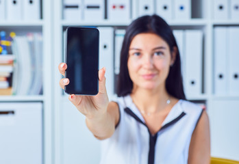 Young smiling business woman showing a blank smartphone screen. Focus on smartphone. Free space for your message.