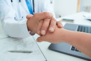 Friendly male doctor's hands holding female patient's hand for encouragement and empathy. Partnership, trust and medical ethics concept. Bad news lessening and support. Patient cheering and support