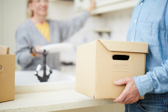 Senior man carrying heavy carton box with domestic stuff while helping his wife with packing and relocating