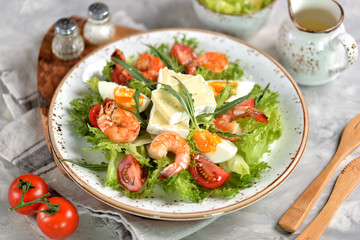 Healthy lettuce salad with arugula, large shrimps, cherry tomatoes, boiled egg, brie cheese and grated parmesan cheese.