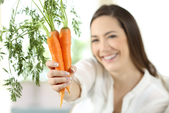 Satisfied woman showing carrots at home