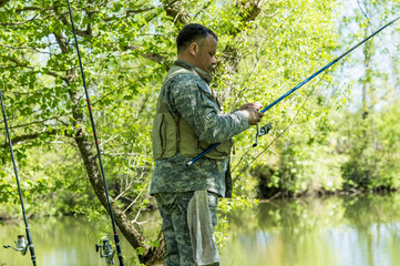 A man in camouflage fishing rod on the river Bank in early summer