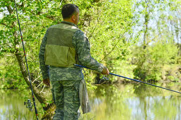 A man in camouflage fishing rod on the river Bank in early summer