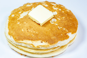 A square of butter laying onto of a stack of golden pancakes on the kitchen table waiting to be eaten