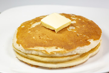 A square of butter laying onto of a stack of golden pancakes on the kitchen table waiting to be eaten