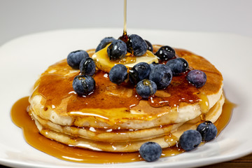 Pouring syrup over the butter on the blueberry stack of pancakes on the kitchen table waiting to be eaten