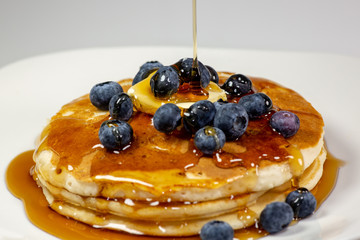 Pouring syrup over the butter on the blueberry stack of pancakes on the kitchen table waiting to be eaten