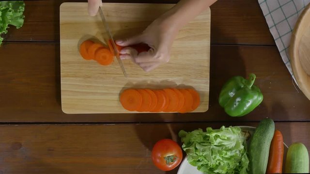 Top view of woman chief making salad healthy food and chopping carrot on cutting board in the kitchen.