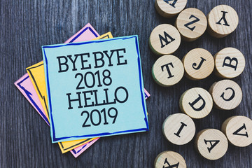 Handwriting text Bye Bye 2018 Hello 2019. Concept meaning Starting new year Motivational message 2018 is over Black wooden deck written sticky note beside some round woody alphabets. © A