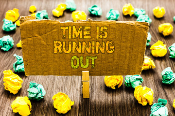 Text sign showing Time Is Running Out. Conceptual photo Deadline is approaching Urgency things cannot wait Paperclip grip cardboard with texts many colorful lobs scattered on wooden desk.
