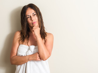 Beautiful middle age woman, wet hair wearing a towel serious face thinking about question, very...