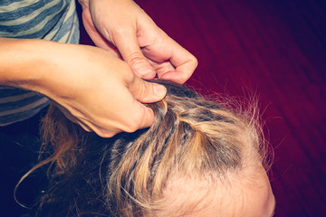 Mom weaves her hair to her daughter, makes her hair at home.