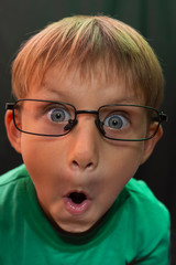 Casual boy with glasses with a stupid expression on his face, looks at the camera, against a dark...