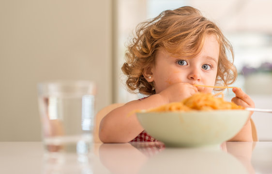 Beautiful blond child eating spaghetti with hands at home