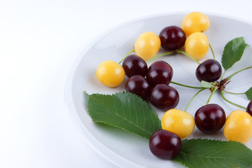 Red and yellow cherries on a white plate, fresh multicolored cherries with green leaves, yellow and red berries in the style of minimalism, vegetarian food