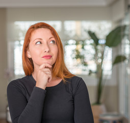 Redhead woman at home serious face thinking about question, very confused idea