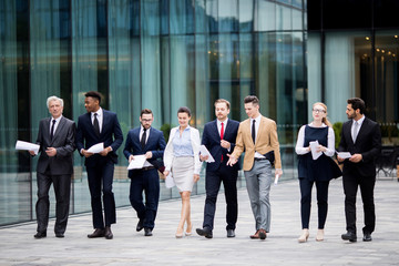 Several business people in elegant suits walking by modern building while having talk with each...