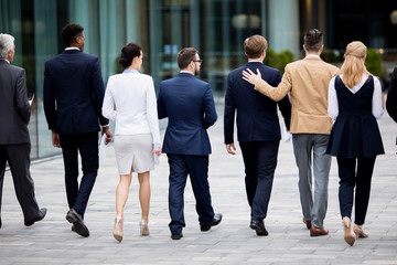 Rear view of elegant employees in suits moving down boulevard in modern city