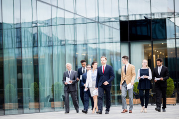 Young confident businesspeople in suits moving along modern glass building