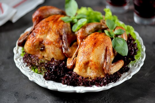 Two baked chicken with lettuce on white plate and black background.