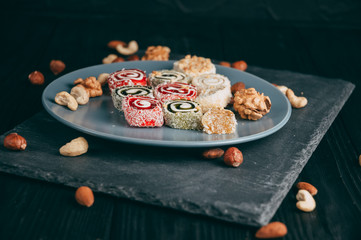 Traditional oriental sweets and nuts: hazelnuts, cashews on a dark wooden background. Turkish dessert is the Rakhat locus. View from above. Place under the text.