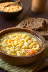 Vegetarian and vegan yellow split pea soup or stew with potato, carrot and celery in wooden bowl, photographed with natural light (Selective Focus, Focus in the middle of the soup)
