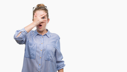 Young blonde business woman peeking in shock covering face and eyes with hand, looking through fingers with embarrassed expression.