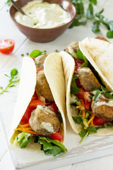Arabic cuisine. Concept of vegetarian food. Delicious fresh homemade vegetarian tortilla with falafel close-up on a wooden kitchen table. Street food, fast food.