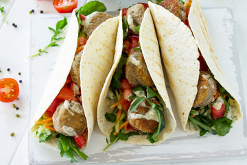 Arabic cuisine. Concept of vegetarian food. Delicious fresh homemade vegetarian tortilla with falafel on a wooden kitchen table. Street food, fast food.