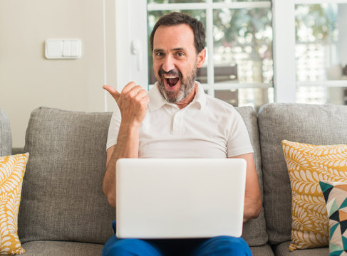 Middle age man using laptop at sofa pointing with hand and finger up with happy face smiling