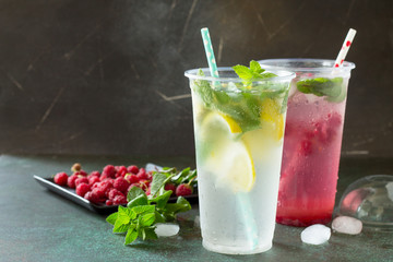 SOFT DRINKS. Refreshing summer drink lemon with mint, ice and raspberry with basil, ice. Glasses with cold and healthy beverage on a stone or slate gray background.