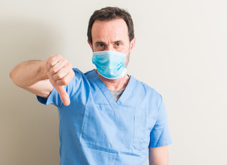 Senior doctor man using mask with angry face, negative sign showing dislike with thumbs down, rejection concept