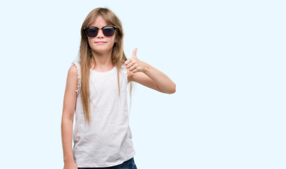 Young blonde toddler wearing sunglasses happy with big smile doing ok sign, thumb up with fingers, excellent sign